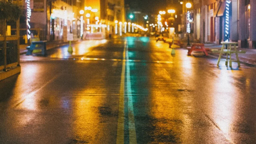 夜の街路に反射する光と雨の路面