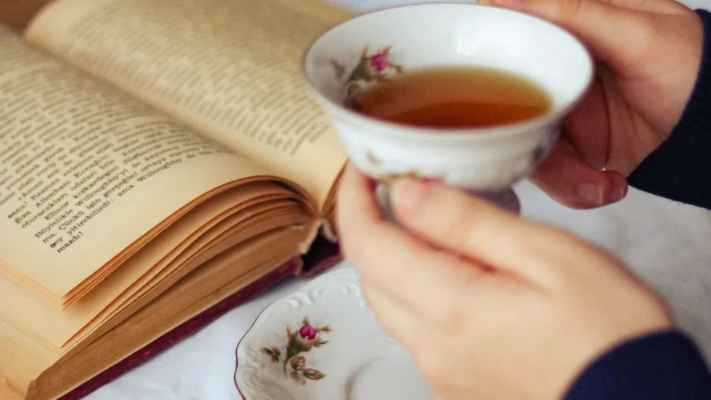 開いた本のそばで紅茶を楽しむ手元